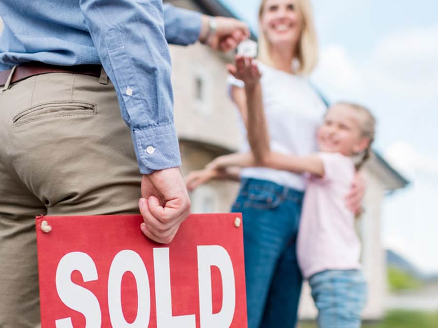 Real Estate Agent holding a sold sign handing keys to a mother and daughter