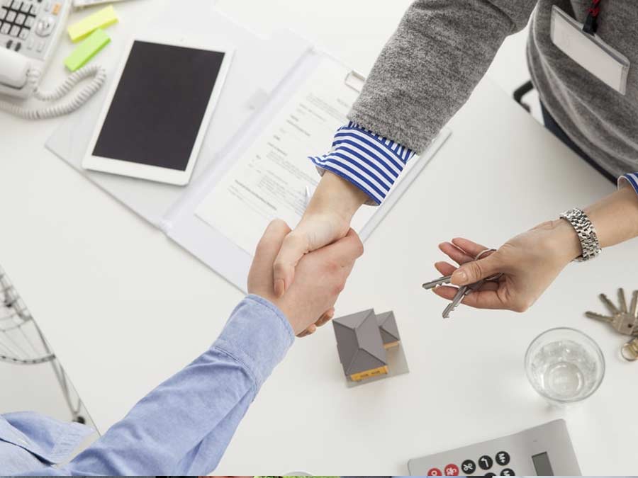 Two people shaking hands over a signed agreement, with one person holding keys